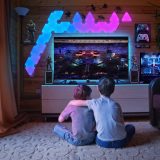 Dos niños sentados en el suelo del salón, de espaldas, viendo en una televisión un estadio iluminado con un ring de boxeo en el centro